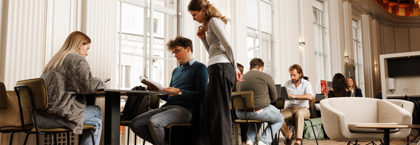 Studenten werken samen en studeren in een stijlvolle common room met hoge plafonds en veel daglicht.
