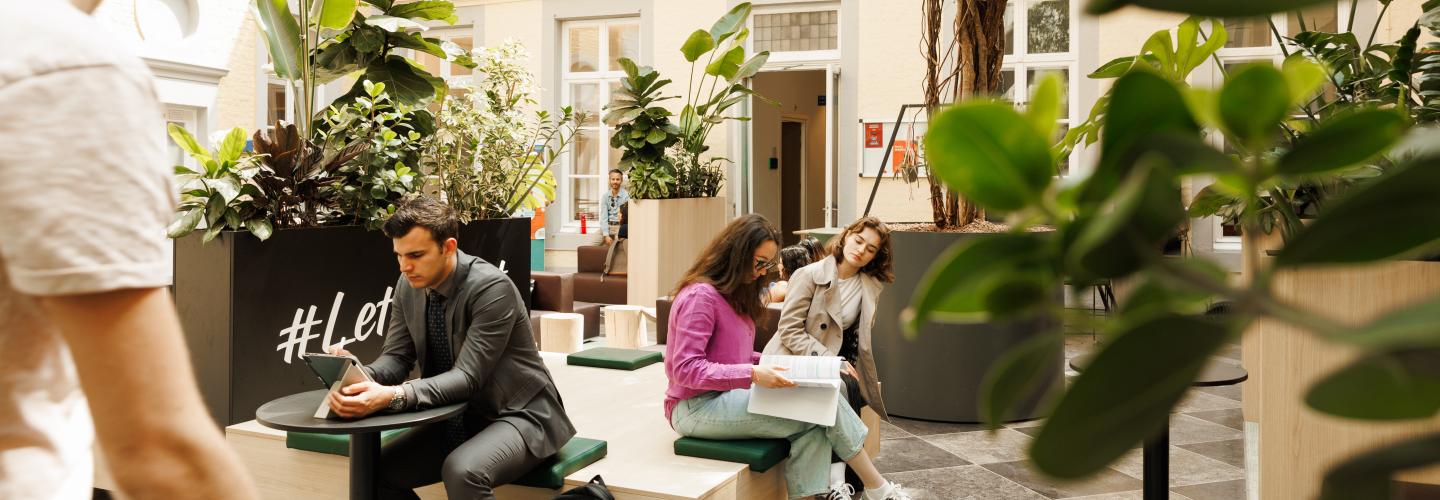 Students studying and chatting in a bright indoor courtyard filled with greenery at the Faculty of Law building on Kapoenstraat.