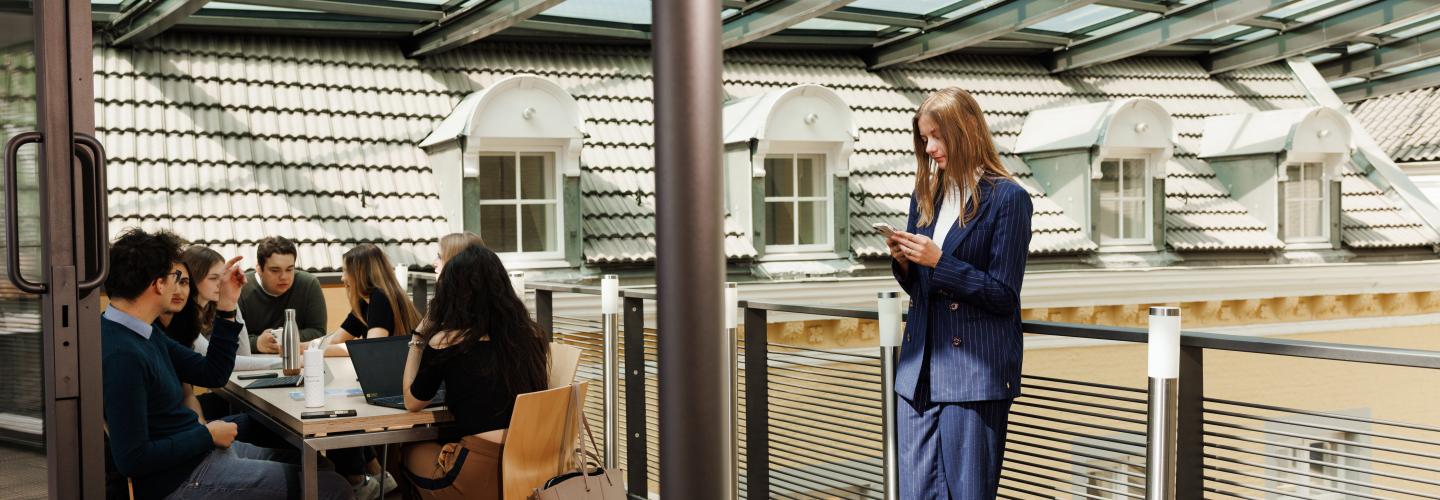 Students studying and discussing on the glass-covered rooftop terrace of the Faculty of Law on Kapoenstraat, overlooking the surrounding rooftops.
