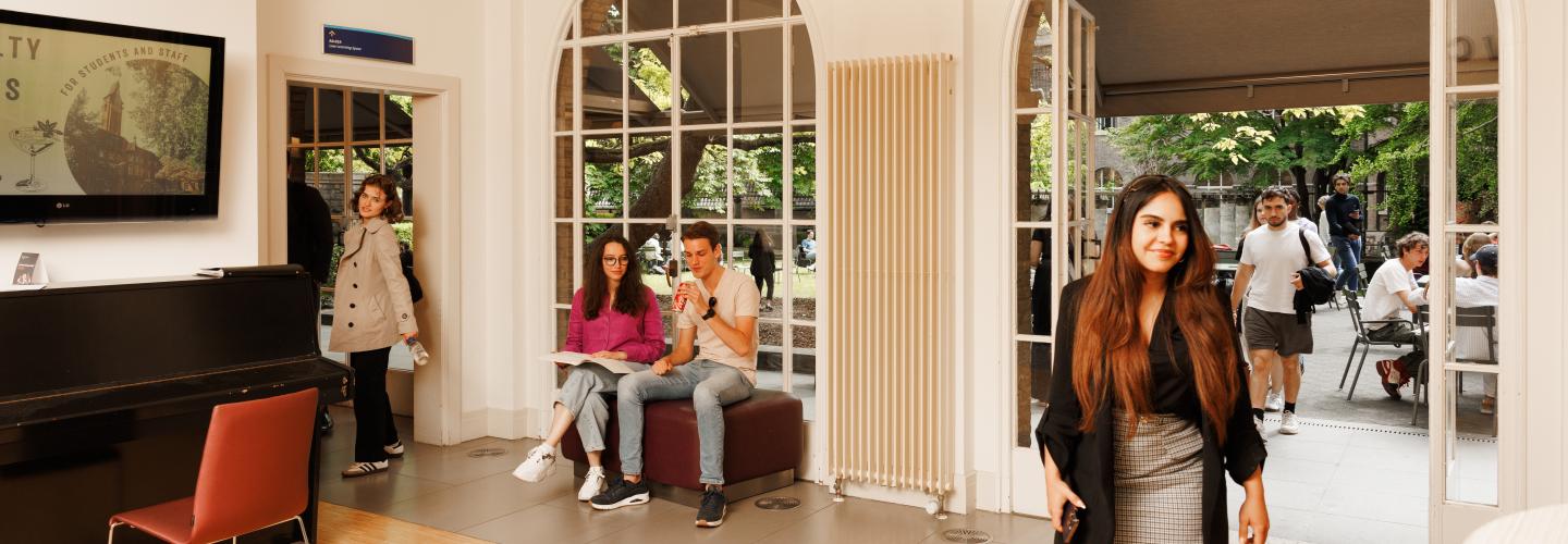Students at the Faculty of Law’s Law Café: one student walks in while others are seated inside and outside, studying and relaxing.