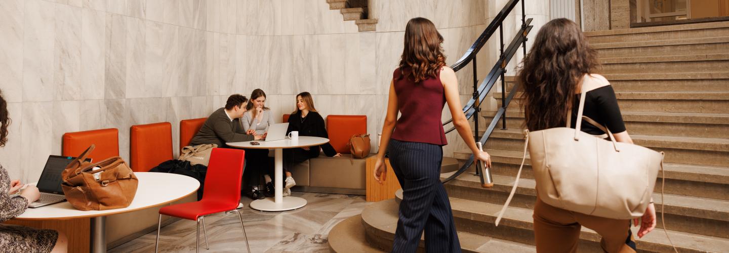 Students working and chatting in the marble hallway of the Lenculenhal, with seating along the wall and a grand staircase in view.