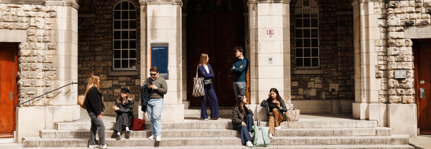 Students sitting and chatting on the steps of the historic entrance of the Faculty of Law on Lenculenstraat in Maastricht.