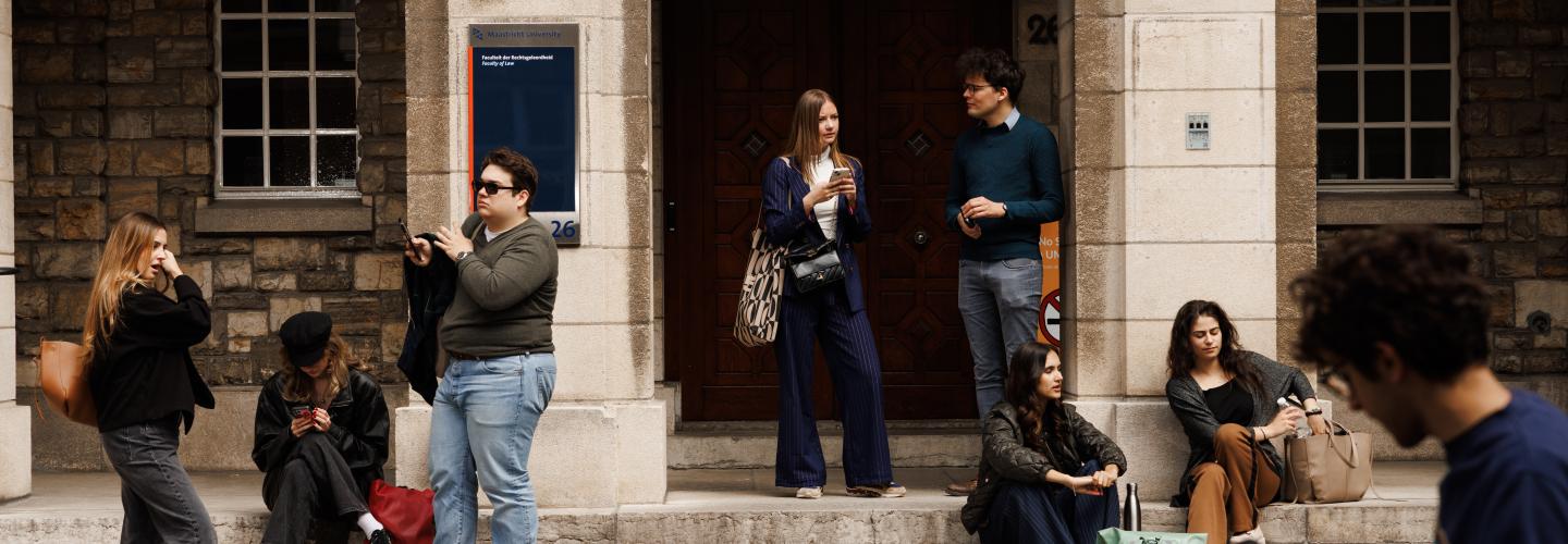 Students standing and sitting on the steps in front of the Faculty of Law entrance on Lenculenstraat, while a cyclist passes by in the foreground.