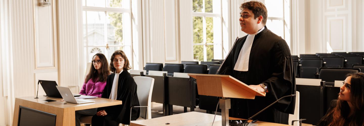Studenten oefenen een rechtszaak in toga tijdens een moot court-sessie aan de rechtenfaculteit van Maastricht University, in een lichte zaal met grote ramen.
