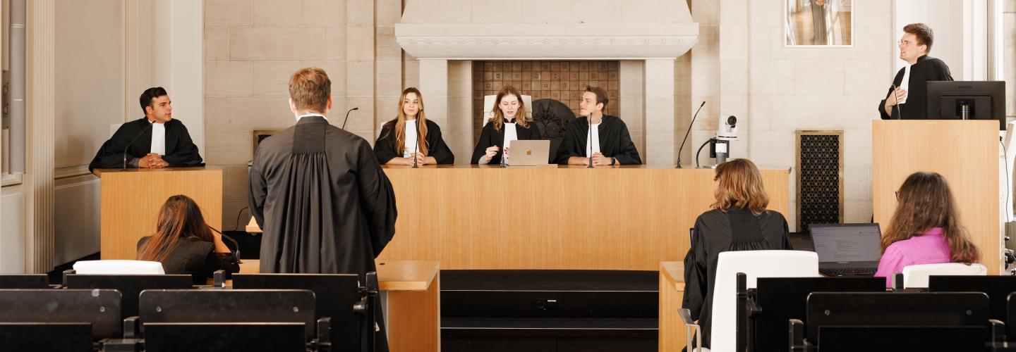 Studenten oefenen in toga een rechtszaak in de Moot Court-zaal van de faculteit, met een rechterspaneel, aanklagers en verdediging.