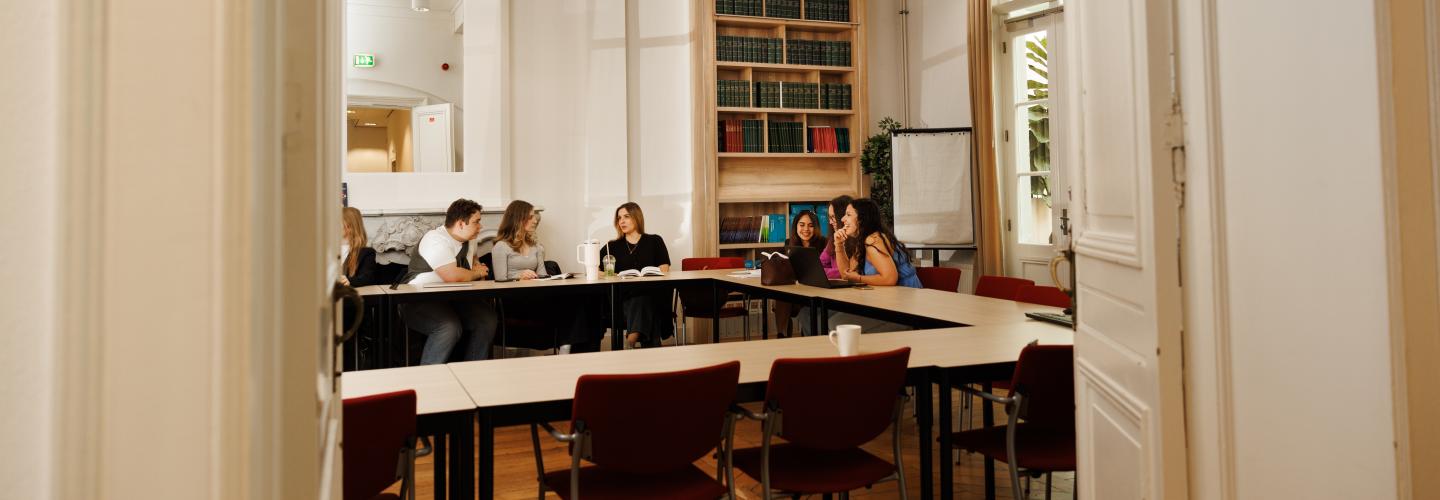 View through a doorway into a tutorial group in the Faculty of Law’s Spiegelzaal, featuring bookshelves, a flipchart, and a classic interior.