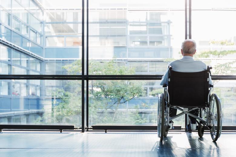 Man in wheelchair looking out of the window of a nursing home