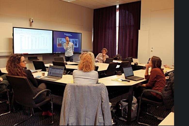 One person giving a presentation and people sitting around the room in a circle