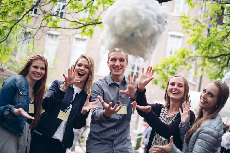 5 Students smiling at the camera and throwing something in the air at Alumni day