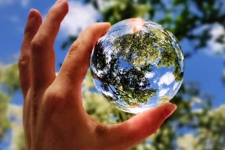 hand holding glass sphere towards sky