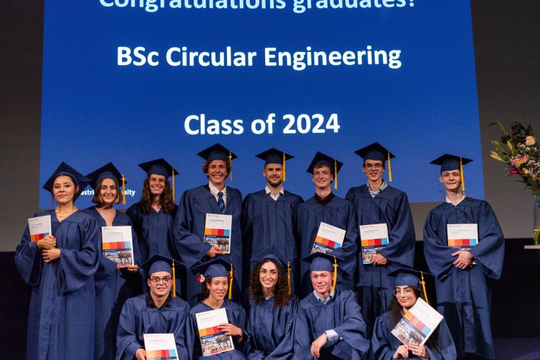 Thirteen students in blue gowns pose with their diploma in hands