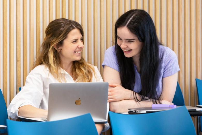 Two seated researchers with one laptop laughing 