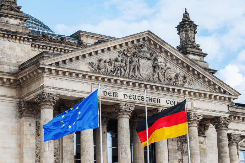 "The Reichstag building in Berlin, Germany, with the European Union and German flags waving in front. The inscription 'Dem Deutschen Volke' is visible on the facade."