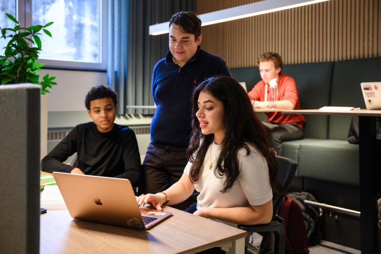 Three students are discussing something at a laptop in the faculty’s learning space, while others work independently in the background.