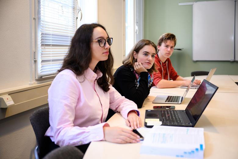 Drie studenten luisteren aandachtig tijdens een PBL-sessie in een onderwijsruimte van de faculteit.