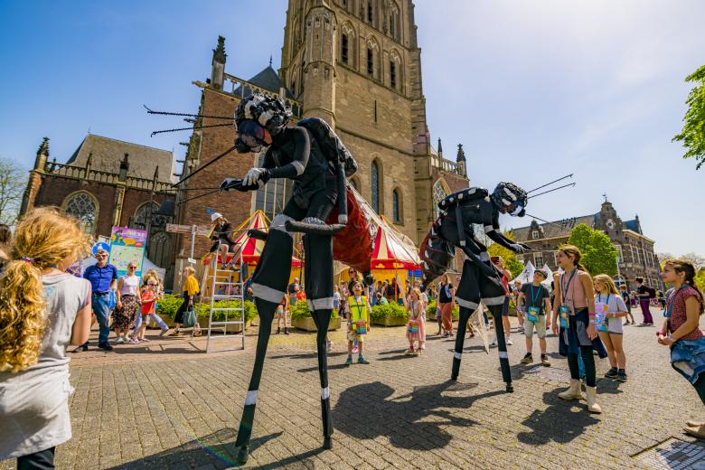 Kinderen op plein Expeditie Next, met mensen in vliegenkostuums op stelten