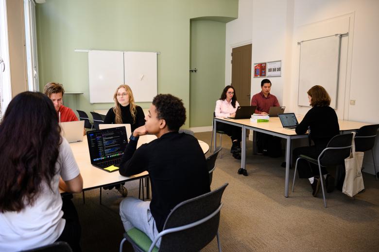 Students participate in a PBL session in groups, seated at two tables in a faculty classroom.