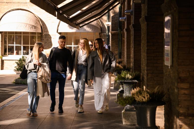 Four students walk together through the faculty’s courtyard, chatting in the sunlight.