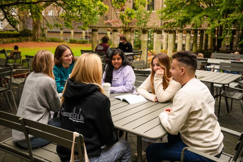 Students sit together at a table in the faculty garden, laughing during an informal study discussion.