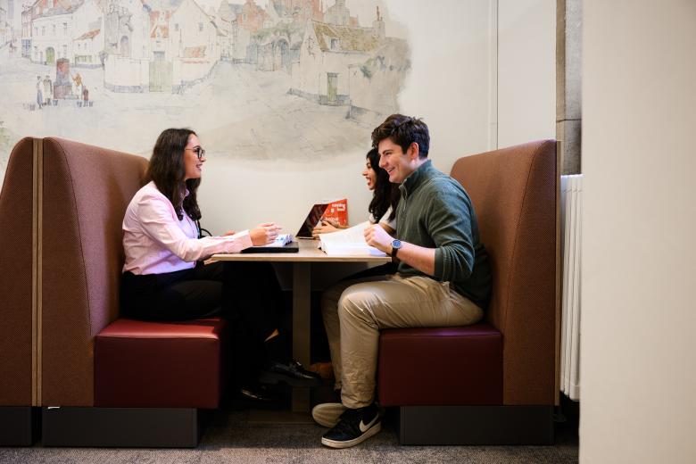 Three students sit together in a booth in the faculty’s learning space, discussing study materials.