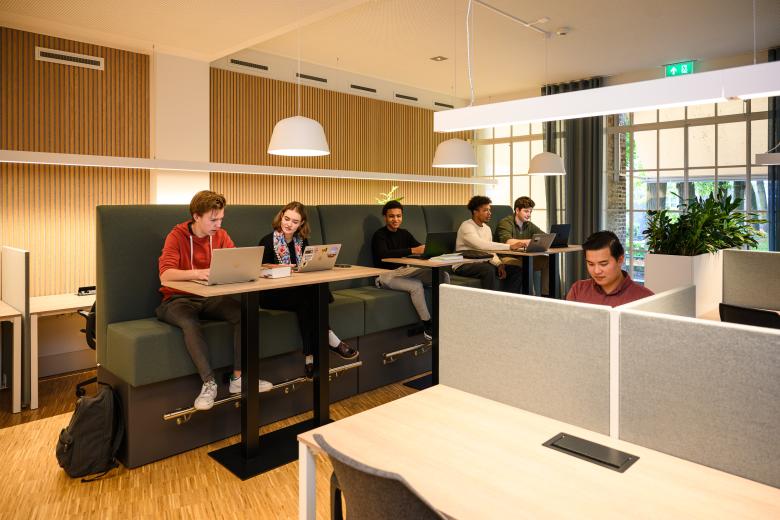 Studenten werken geconcentreerd aan individuele en gezamenlijke werkplekken in de learning space van de faculteit.