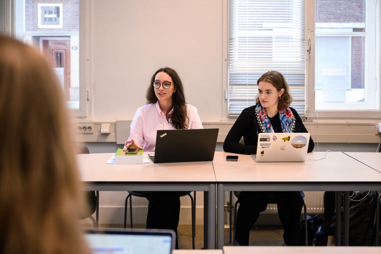 Two students sit at the table during a PBL session, attentively listening to a group member outside the frame.