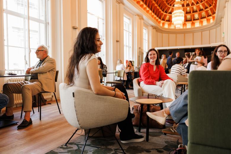 Studenten en staf in gesprek en ontspannen sfeer in de common room van de rechtenfaculteit, met hoge ramen, warme verlichting en een karakteristiek houten plafond.