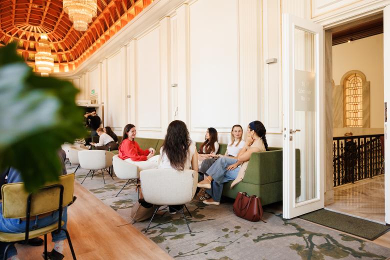 Students relaxing and chatting in the Faculty of Law's Common Room, featuring the iconic wooden ceiling and chandeliers.