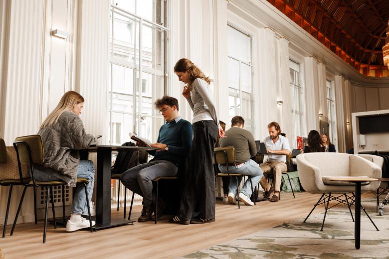 Studenten werken samen en studeren in een stijlvolle common room met hoge plafonds en veel daglicht.