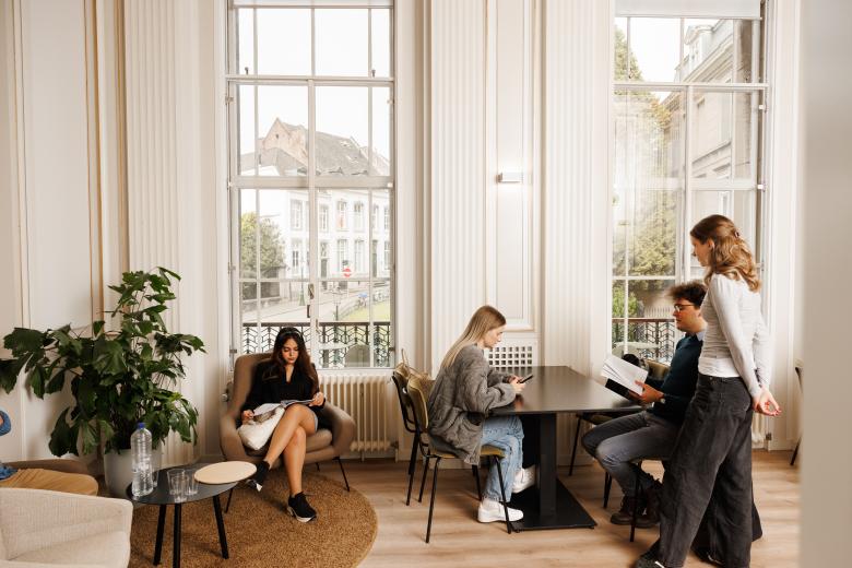 Studenten ontspannen en studeren in een lichte en elegante common room met uitzicht op de binnenstad van Maastricht.