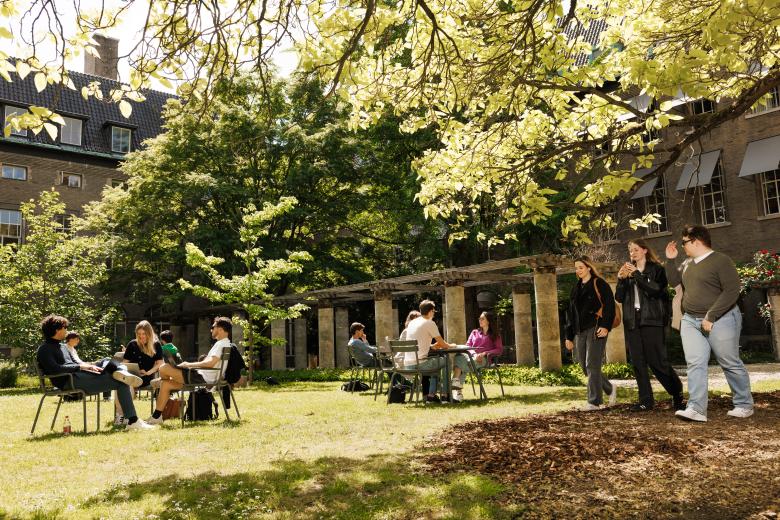 Students sitting and walking in the courtyard garden of the Faculty of Law in Maastricht on a sunny day, surrounded by greenery and historic buildings.