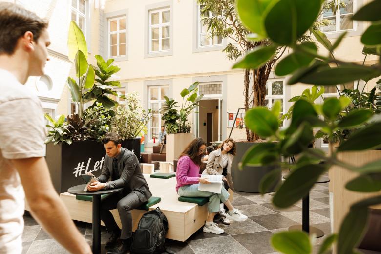 Students studying and chatting in a bright indoor courtyard filled with greenery at the Faculty of Law building on Kapoenstraat.