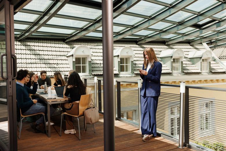 Students studying and discussing on the glass-covered rooftop terrace of the Faculty of Law on Kapoenstraat, overlooking the surrounding rooftops.