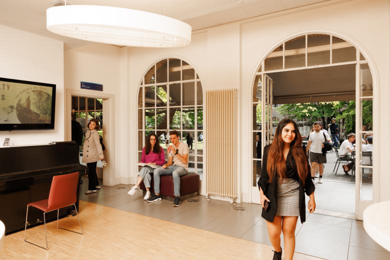 Students at the Faculty of Law’s Law Café: one student walks in while others are seated inside and outside, studying and relaxing.
