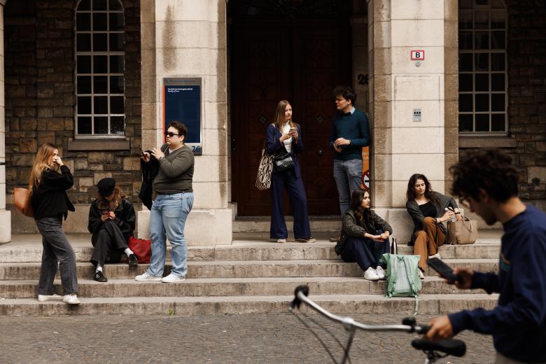 Students standing and sitting on the steps in front of the Faculty of Law entrance on Lenculenstraat, while a cyclist passes by in the foreground.