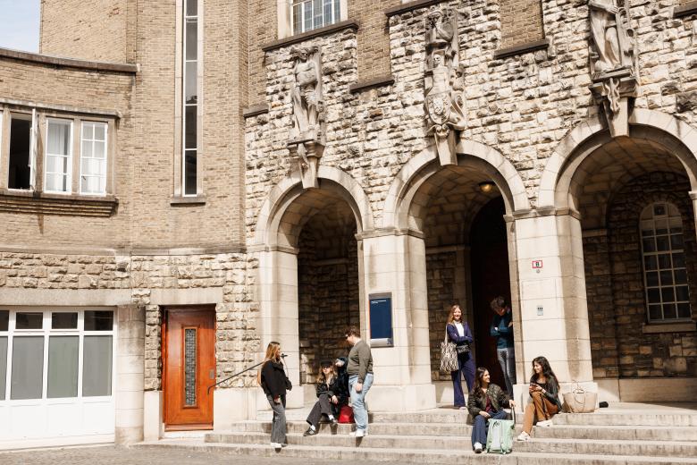 Students sitting and chatting on the steps in front of the monumental entrance of the Faculty of Law on Lenculenstraat in Maastricht, beneath sculpted figures on the facade.