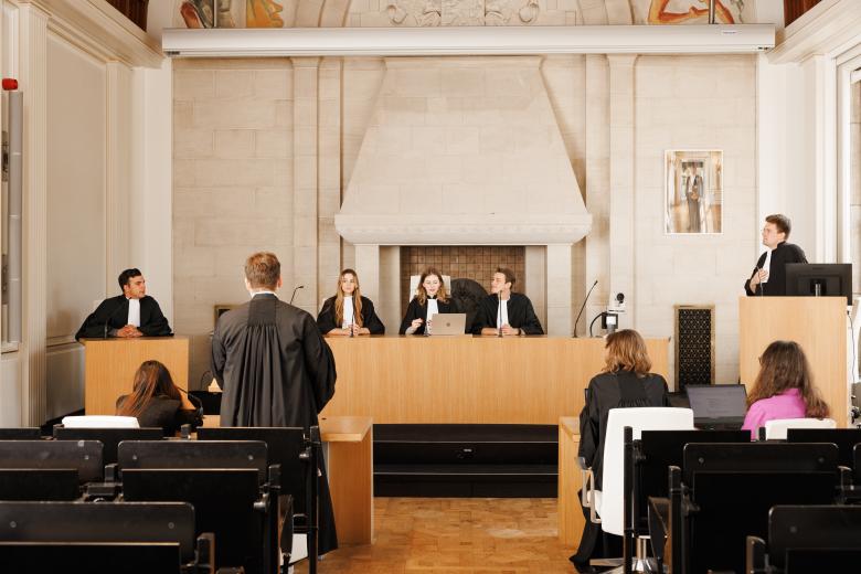 Studenten oefenen in toga een rechtszaak in de Moot Court-zaal van de faculteit, met een rechterspaneel, aanklagers en verdediging.