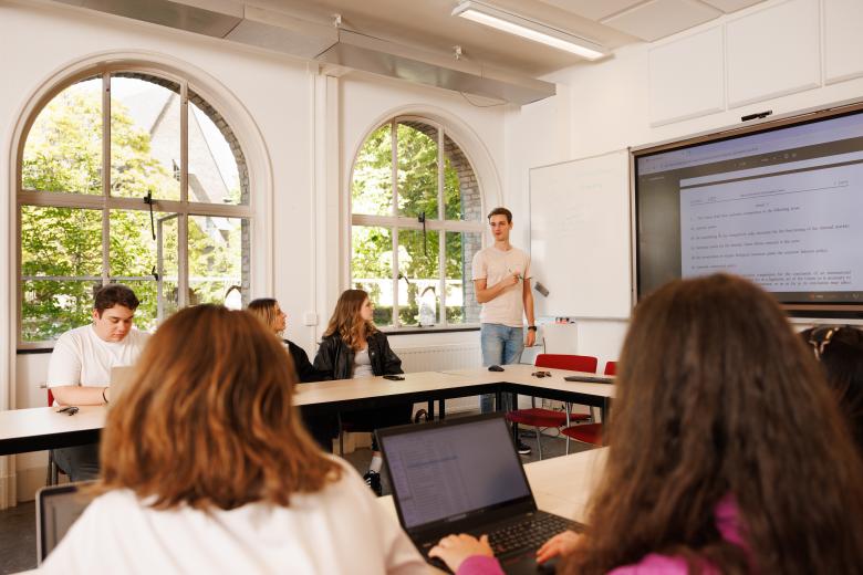 Student geeft een presentatie voor een groep medestudenten tijdens een PBL-sessie, met aantekeningen op het whiteboard en juridische tekst geprojecteerd op het scherm.