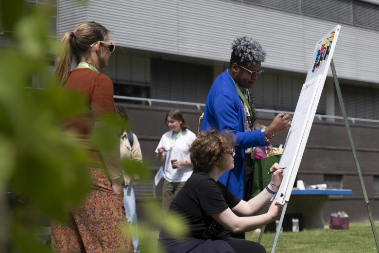 Staff and students write reasons for Pride month on a flipover at Pride Month flag raising event