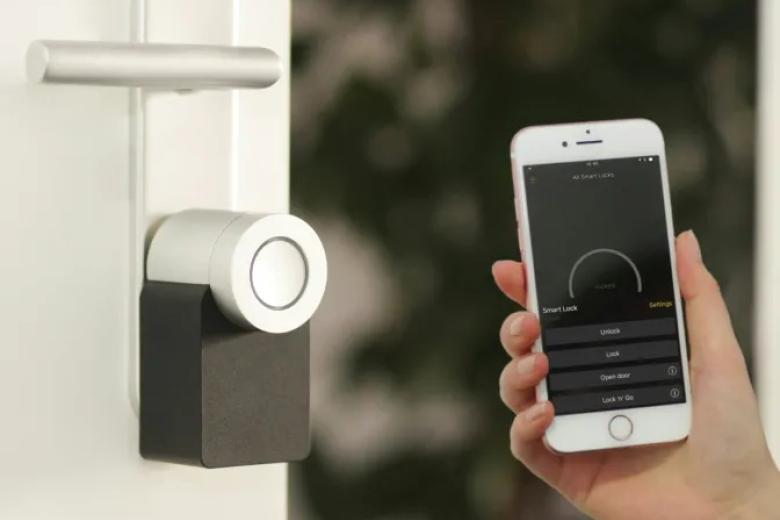 A smart home technology app is open on a smartphone next to a door lock.