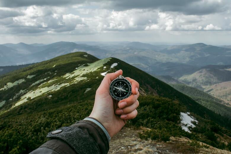 A hand holding a compass in the mountains