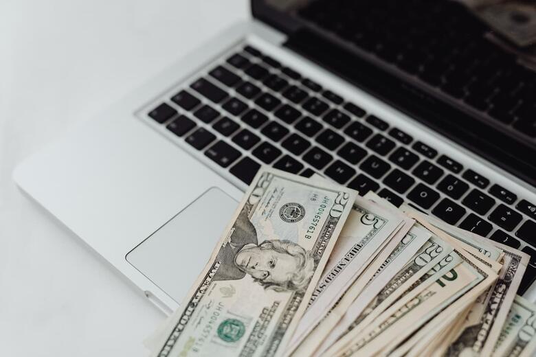 A laptop with a fan of cash money on it.