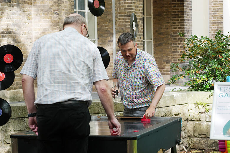 Twee medewerkers die airhockey spelen in de tuin van de faculteit tijdens de staf barbecue.